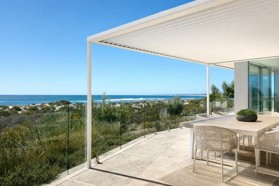 White steel patio over a limestone terrace with dining chairs, looking out over coastal dunes to the ocean